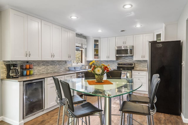 kitchen with beverage cooler, backsplash, appliances with stainless steel finishes, white cabinetry, and hardwood / wood-style flooring