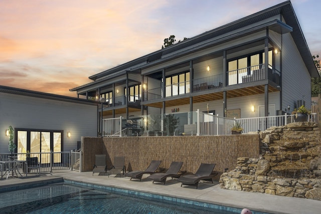 back house at dusk featuring a fenced in pool, a balcony, and a patio area