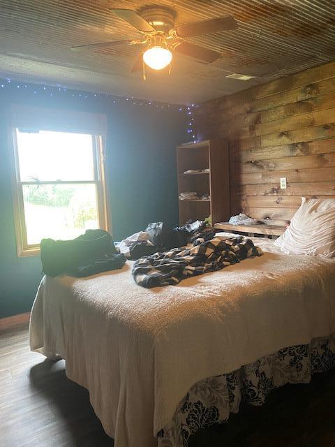 bedroom featuring wood-type flooring, wooden walls, and ceiling fan