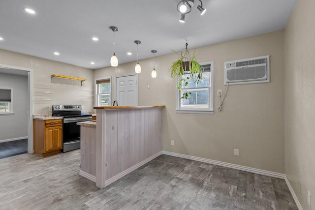 kitchen featuring a wall unit AC, wood-type flooring, decorative light fixtures, kitchen peninsula, and stainless steel electric range