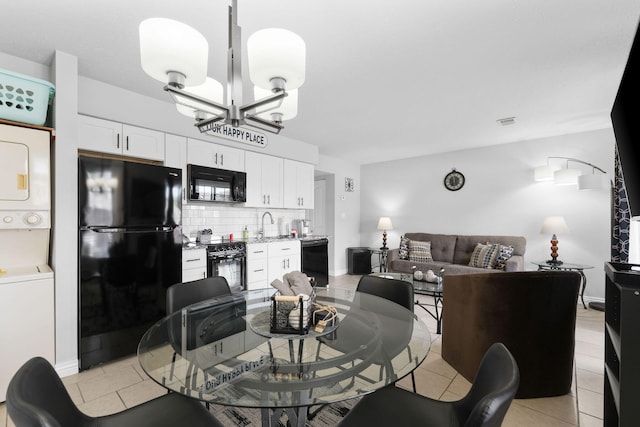 tiled dining area featuring stacked washer and clothes dryer and a chandelier