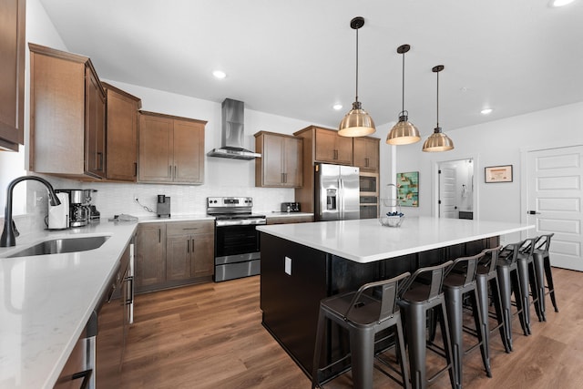 kitchen featuring wall chimney range hood, decorative light fixtures, sink, appliances with stainless steel finishes, and a center island