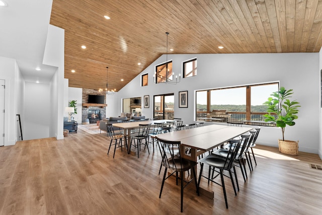 dining room with wood ceiling, light hardwood / wood-style floors, high vaulted ceiling, and a stone fireplace