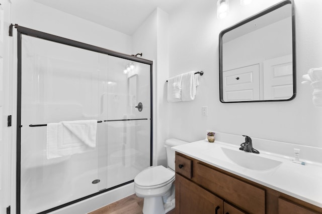 bathroom featuring hardwood / wood-style flooring, a shower with shower door, vanity, and toilet