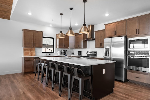 kitchen featuring a kitchen island, stainless steel appliances, wall chimney exhaust hood, dark hardwood / wood-style flooring, and pendant lighting