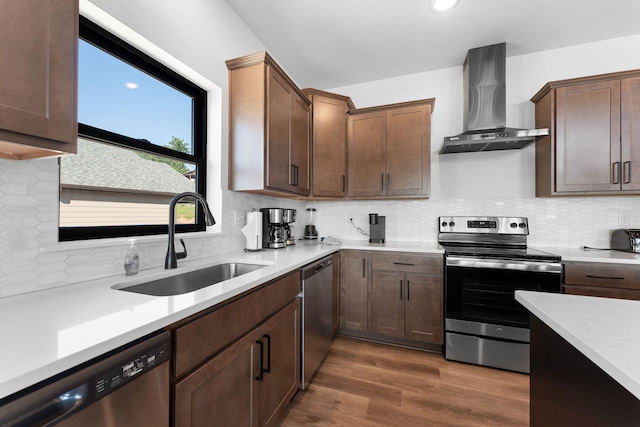 kitchen with sink, tasteful backsplash, wall chimney range hood, appliances with stainless steel finishes, and dark hardwood / wood-style flooring