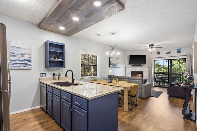 kitchen with light stone countertops, dark hardwood / wood-style floors, blue cabinetry, sink, and a fireplace