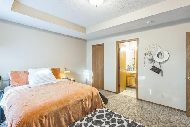 bedroom featuring connected bathroom, a raised ceiling, a textured ceiling, and light colored carpet