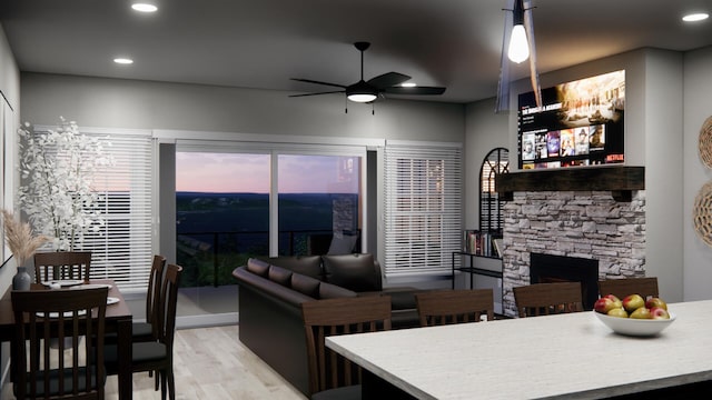 living room with ceiling fan, a stone fireplace, and light hardwood / wood-style flooring