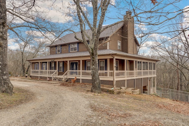 farmhouse featuring dirt driveway, a chimney, roof with shingles, covered porch, and fence