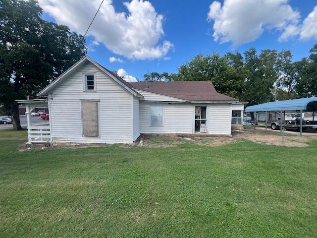 rear view of property with a carport and a yard