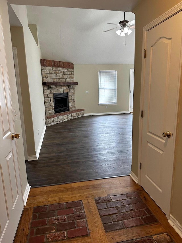 unfurnished living room with a stone fireplace, ceiling fan, and dark wood-type flooring