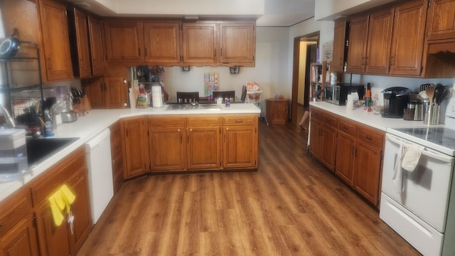 kitchen with kitchen peninsula, white appliances, sink, and wood-type flooring