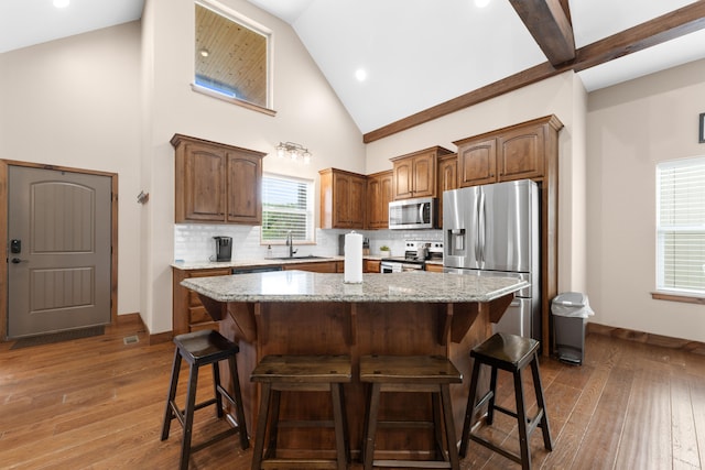 kitchen with high vaulted ceiling, appliances with stainless steel finishes, a kitchen island, and a breakfast bar