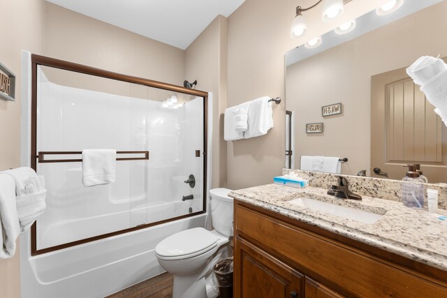 full bathroom featuring vanity, hardwood / wood-style floors, combined bath / shower with glass door, and toilet