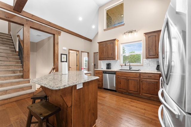 kitchen featuring stainless steel appliances, a sink, a center island, decorative backsplash, and high vaulted ceiling
