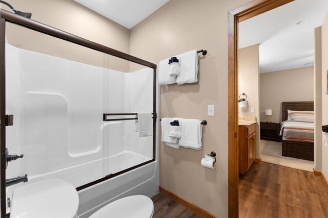 full bathroom featuring hardwood / wood-style flooring, shower / bath combination with glass door, vanity, and toilet