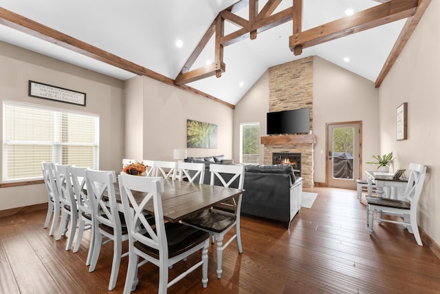dining room featuring wood-type flooring, a stone fireplace, beam ceiling, and baseboards