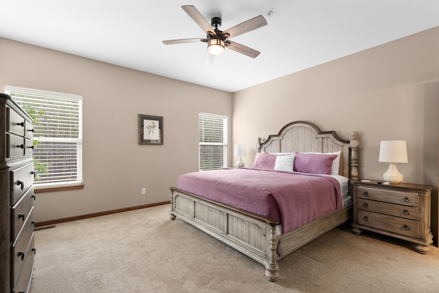 bedroom featuring multiple windows, a ceiling fan, baseboards, and light carpet
