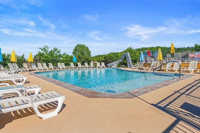 community pool featuring a water slide, fence, and a patio area
