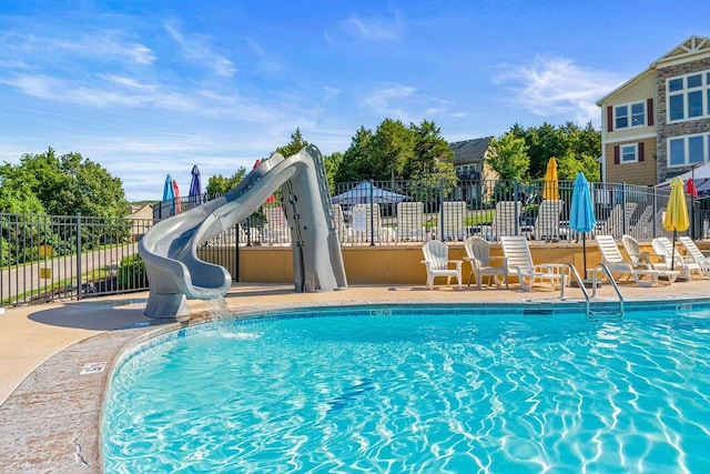 pool with a water slide, fence, and a patio area