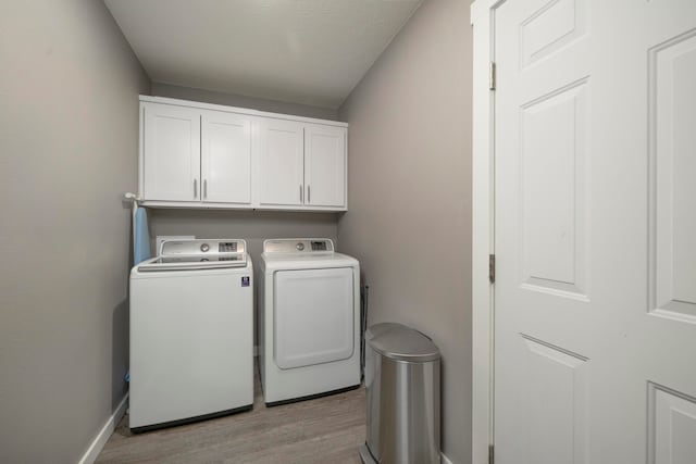 clothes washing area featuring cabinets, light hardwood / wood-style flooring, and washer and dryer