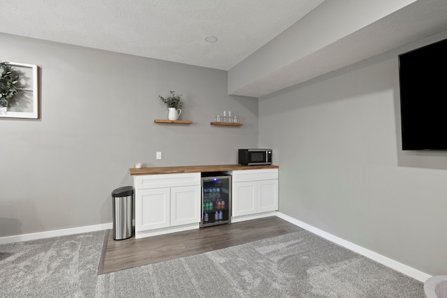 bar with wood counters, white cabinetry, a textured ceiling, dark carpet, and beverage cooler