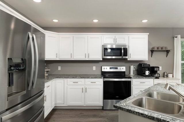 kitchen with appliances with stainless steel finishes, sink, white cabinets, dark hardwood / wood-style flooring, and dark stone counters