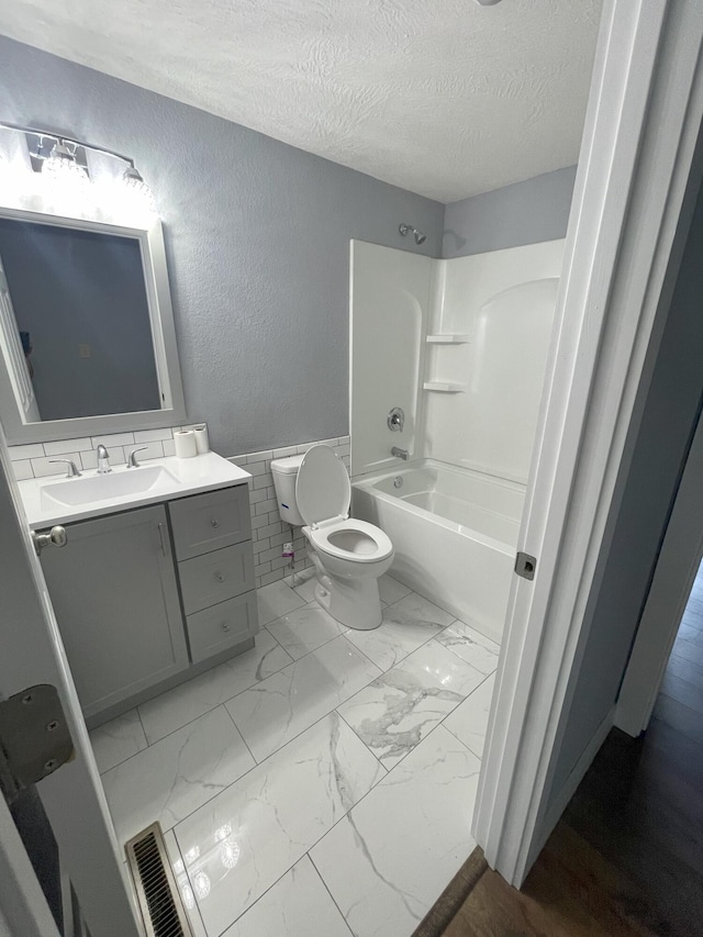 full bathroom featuring toilet, vanity, a textured ceiling, and washtub / shower combination