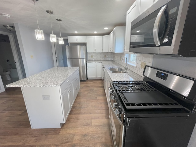 kitchen with sink, stainless steel appliances, a kitchen island, tasteful backsplash, and white cabinets