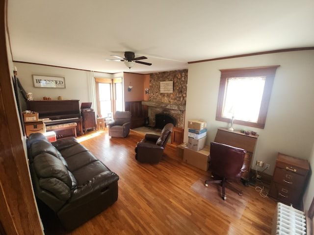 living room with ceiling fan, radiator, hardwood / wood-style floors, a stone fireplace, and ornamental molding