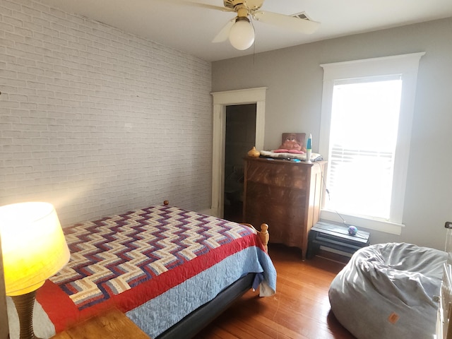 bedroom featuring ceiling fan, hardwood / wood-style floors, and brick wall