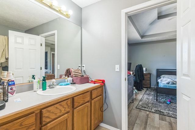ensuite bathroom with baseboards, wood finished floors, ensuite bath, and vanity