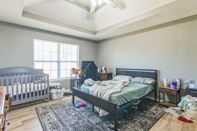 bedroom with hardwood / wood-style flooring, ceiling fan, baseboards, and a tray ceiling