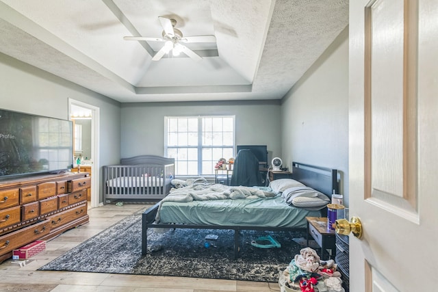 bedroom featuring ceiling fan, a textured ceiling, light wood-type flooring, and a raised ceiling