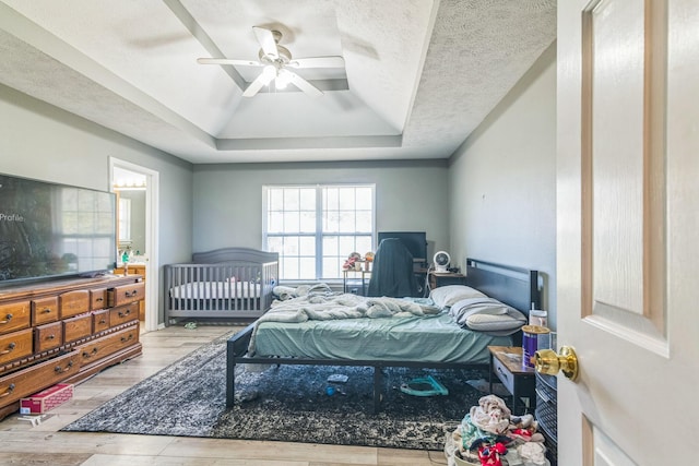 bedroom featuring a tray ceiling, wood finished floors, a textured ceiling, and a ceiling fan