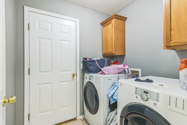 laundry room with a textured ceiling, washer and dryer, light tile patterned floors, and cabinets