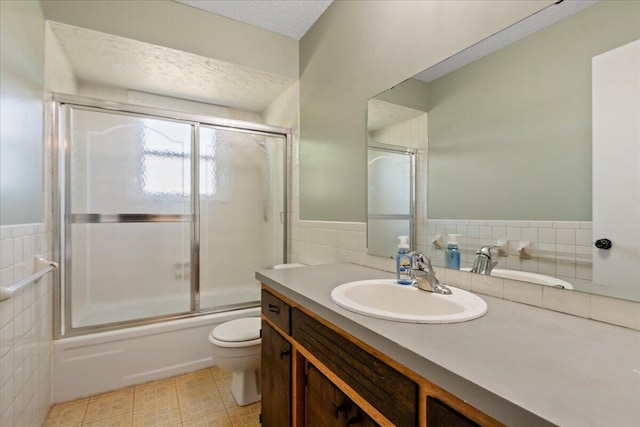 full bathroom featuring vanity, a textured ceiling, bath / shower combo with glass door, tile walls, and toilet