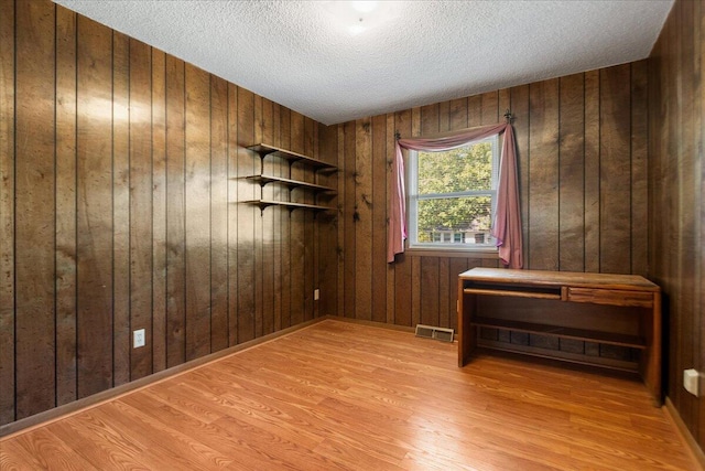 spare room with wood walls, light hardwood / wood-style flooring, and a textured ceiling