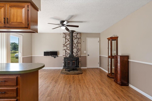 unfurnished living room with ceiling fan, a textured ceiling, light hardwood / wood-style flooring, and a wood stove