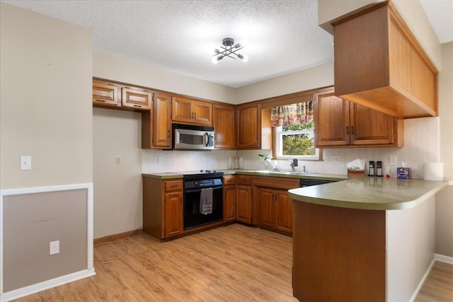 kitchen featuring kitchen peninsula, light wood-type flooring, black oven, and a textured ceiling