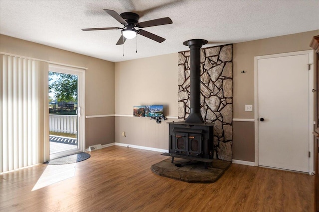 unfurnished living room with ceiling fan, hardwood / wood-style flooring, a textured ceiling, and a wood stove