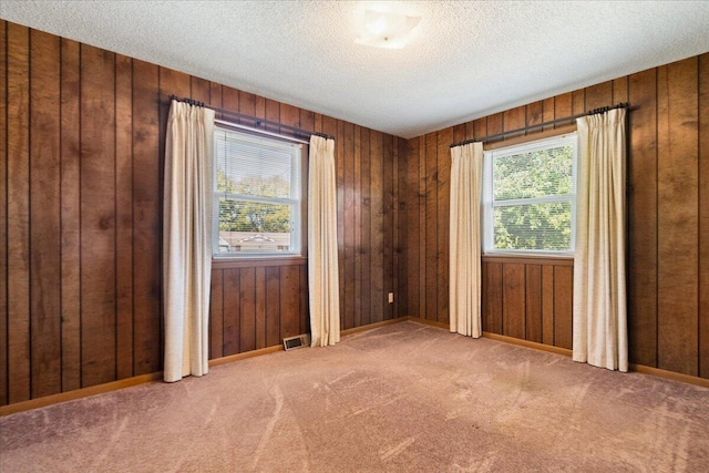 carpeted spare room featuring a textured ceiling and wooden walls