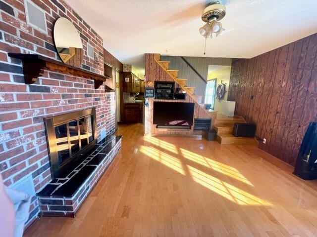 living room with a brick fireplace, wooden walls, wood-type flooring, and ceiling fan