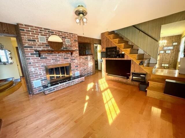 living room with hardwood / wood-style floors, a brick fireplace, and wood walls