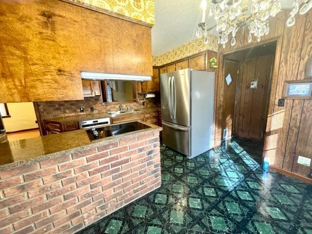 kitchen featuring wooden walls, stainless steel fridge, black electric stovetop, kitchen peninsula, and an inviting chandelier