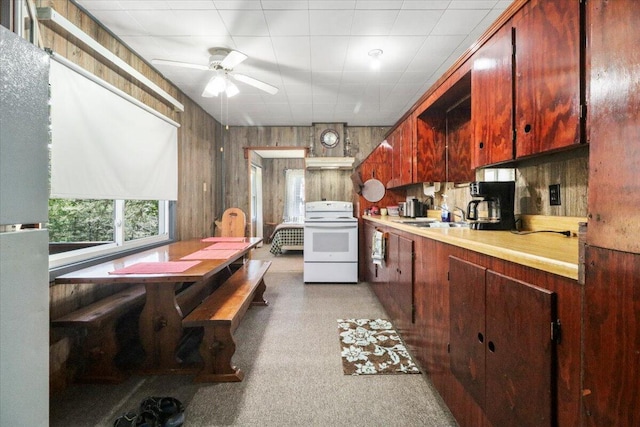kitchen featuring a sink, white electric range, a ceiling fan, wood walls, and light countertops