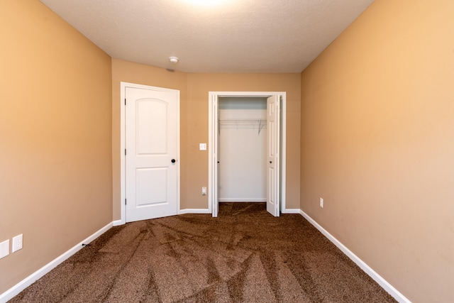 unfurnished bedroom featuring dark carpet, a textured ceiling, and a closet