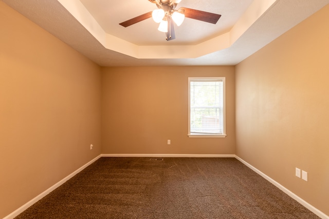 carpeted spare room featuring a tray ceiling and ceiling fan