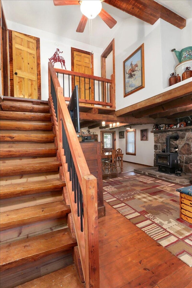 stairway with ceiling fan, hardwood / wood-style flooring, rustic walls, and a wood stove